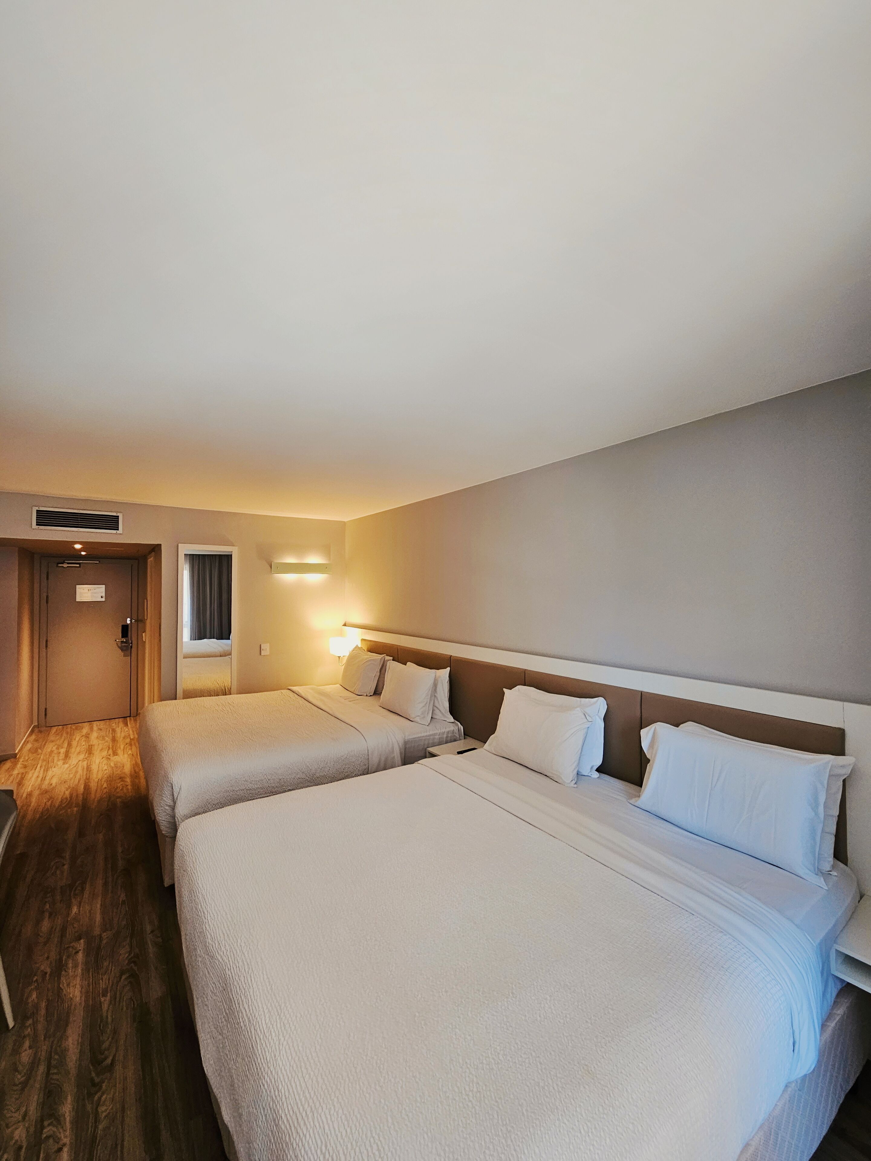 Ett hotellrum med två sängar, ett trägolv, en dörr och en nattlampa.