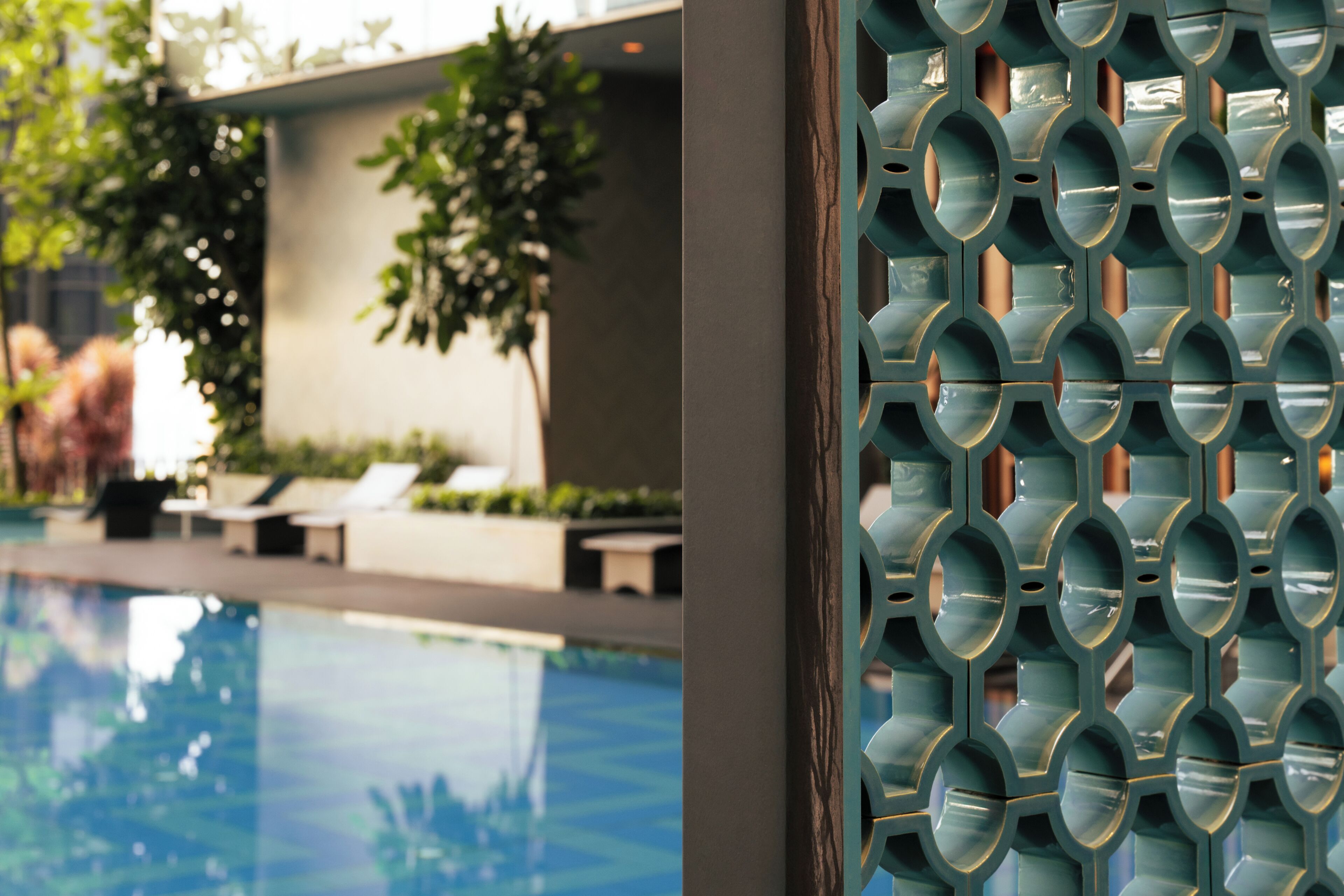 Una piscina con una valla de diseño geométrico, sillas de descanso y follaje al fondo.
