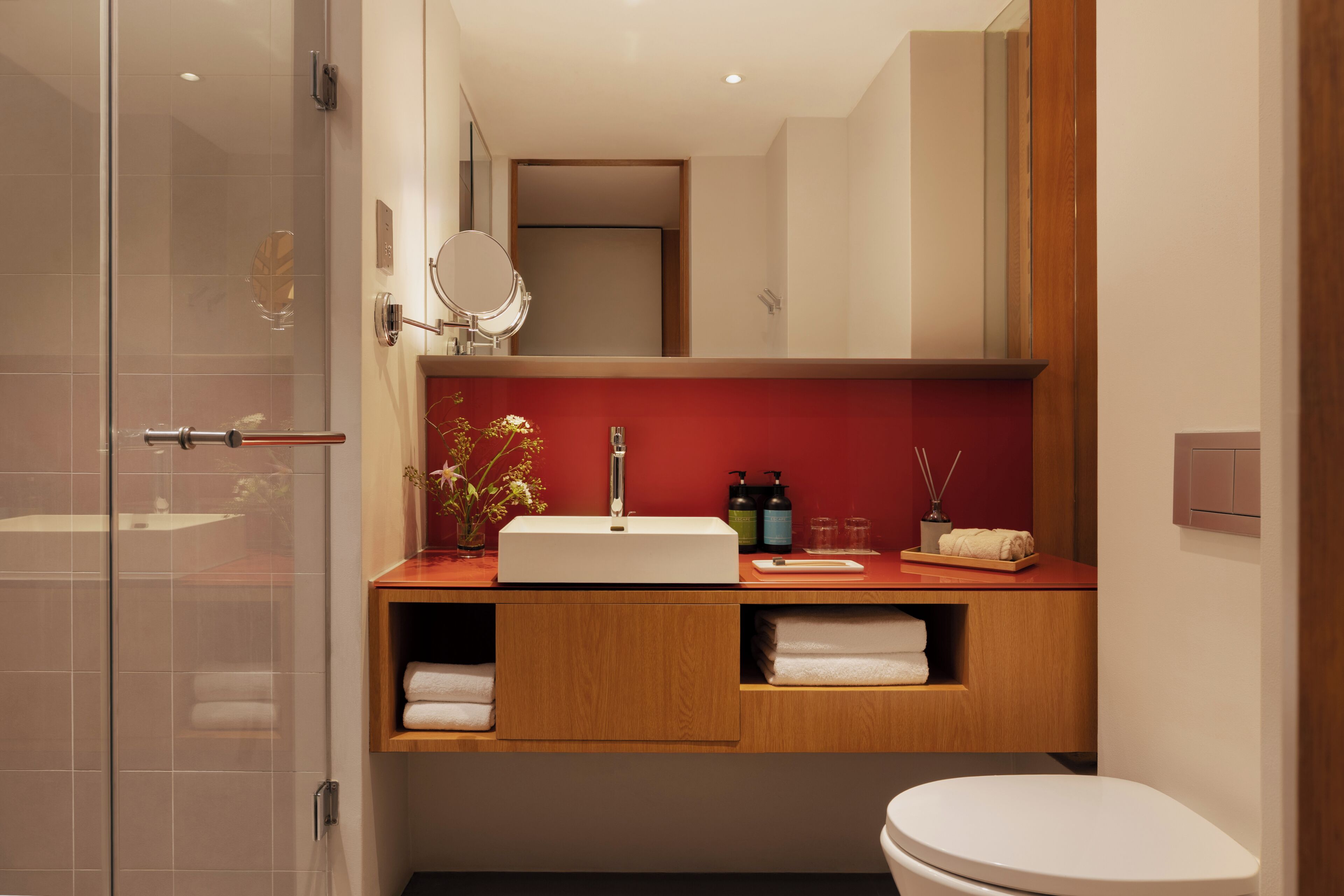 Un baño moderno con cabina de ducha de vidrio, tocador de madera con lavabo blanco y un inodoro blanco.