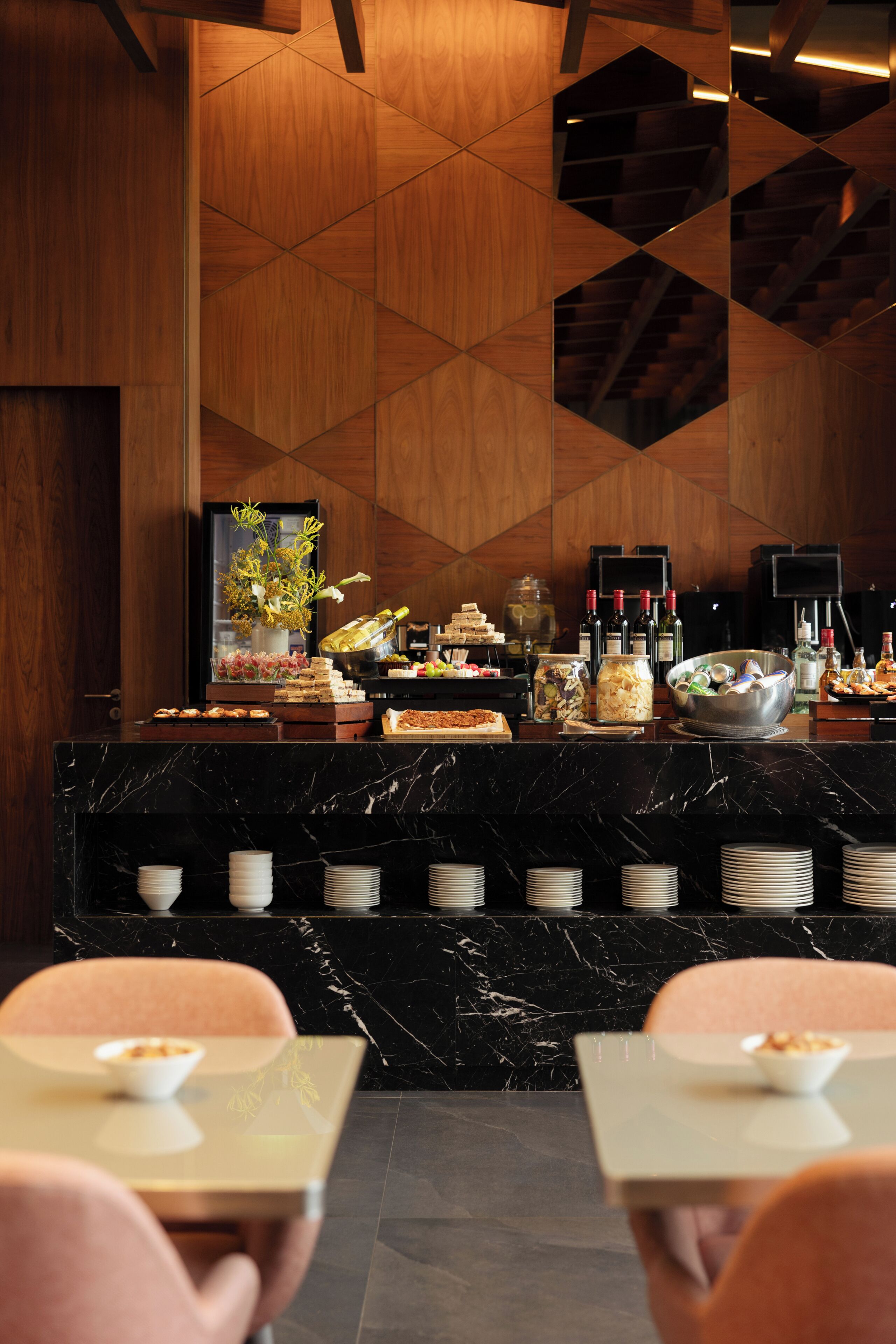 A hotel reception area with a marble counter, a flower arrangement, and a variety of food and drink options.