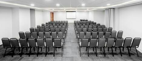 A conference room with rows of chairs, a projector screen, and a carpeted floor.