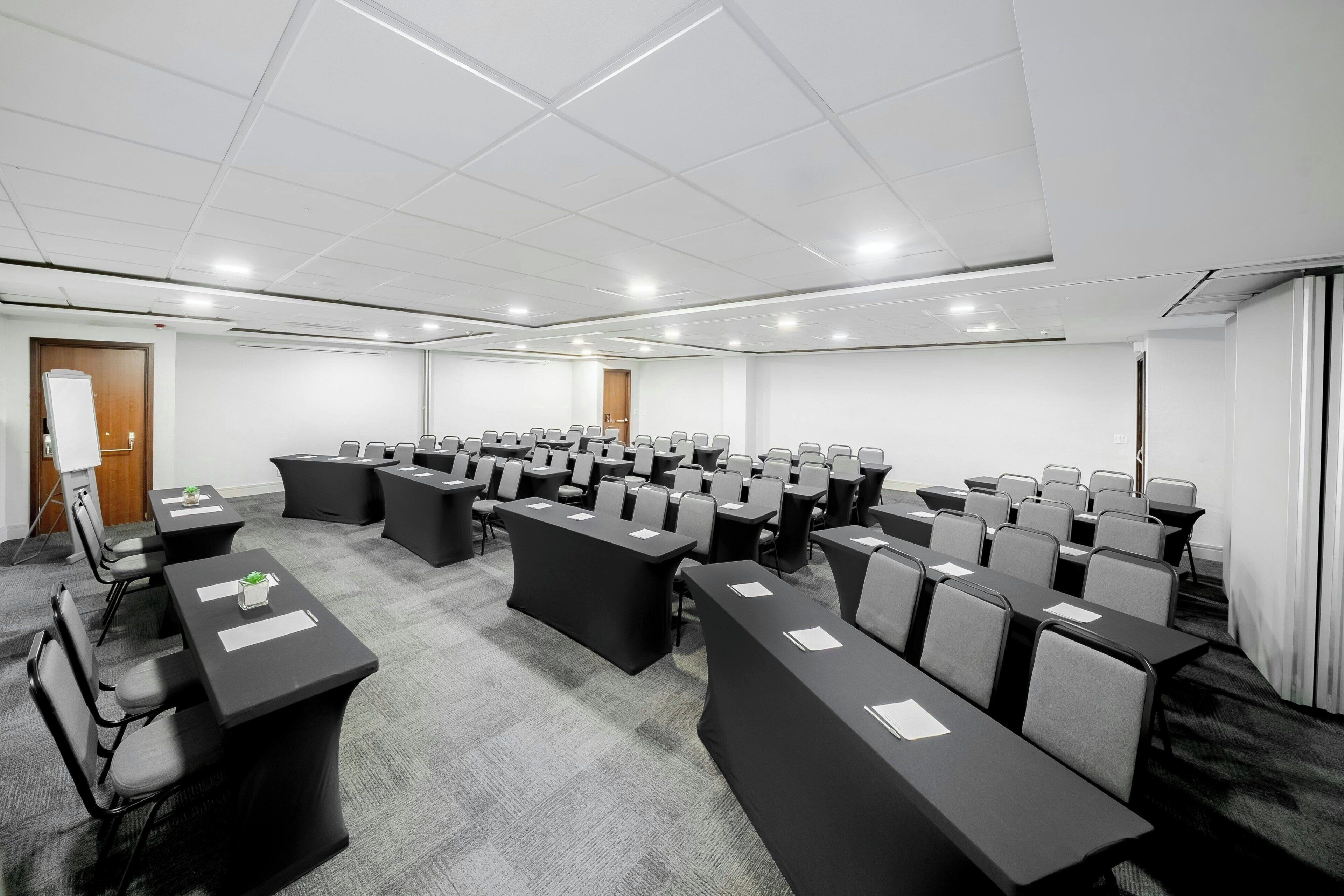 Un salón de conferencias con varias mesas y sillas, paredes blancas y suelo alfombrado.