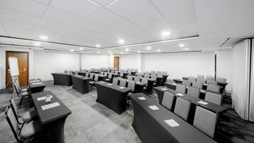 Un salón de conferencias con varias mesas y sillas, paredes blancas y suelo alfombrado.