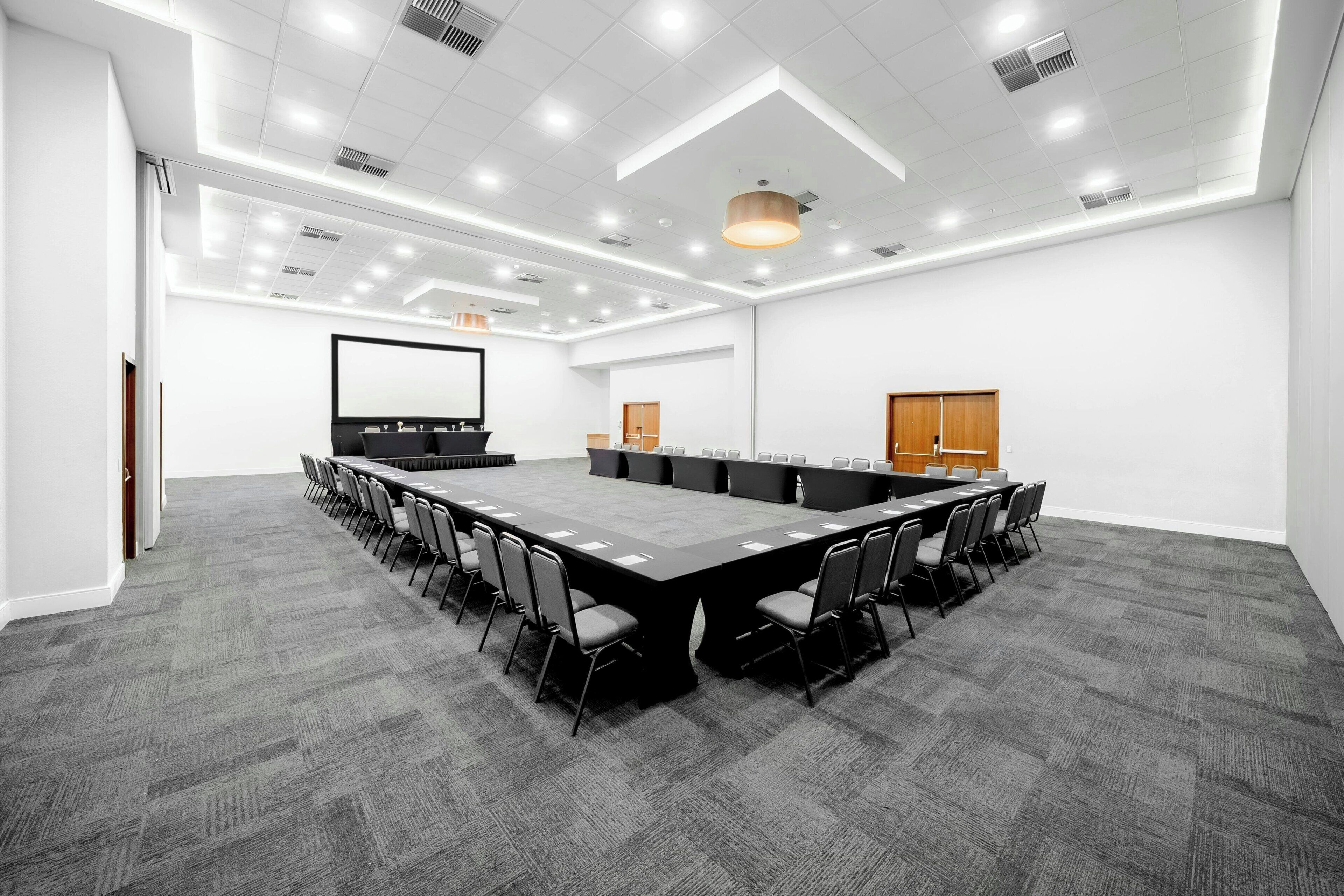 Una sala de conferencias con una larga mesa, sillas, una pantalla de proyector y un armario de madera.