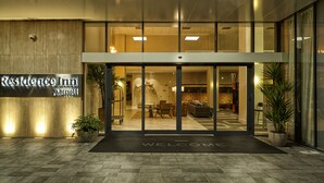 A modern hotel entrance with a 'Welcome' mat, a reception desk, and a seating area visible through the glass doors. - Residence Inn by Marriott Rio de Janeiro Barra da Tijuca (Rio de Janeiro)