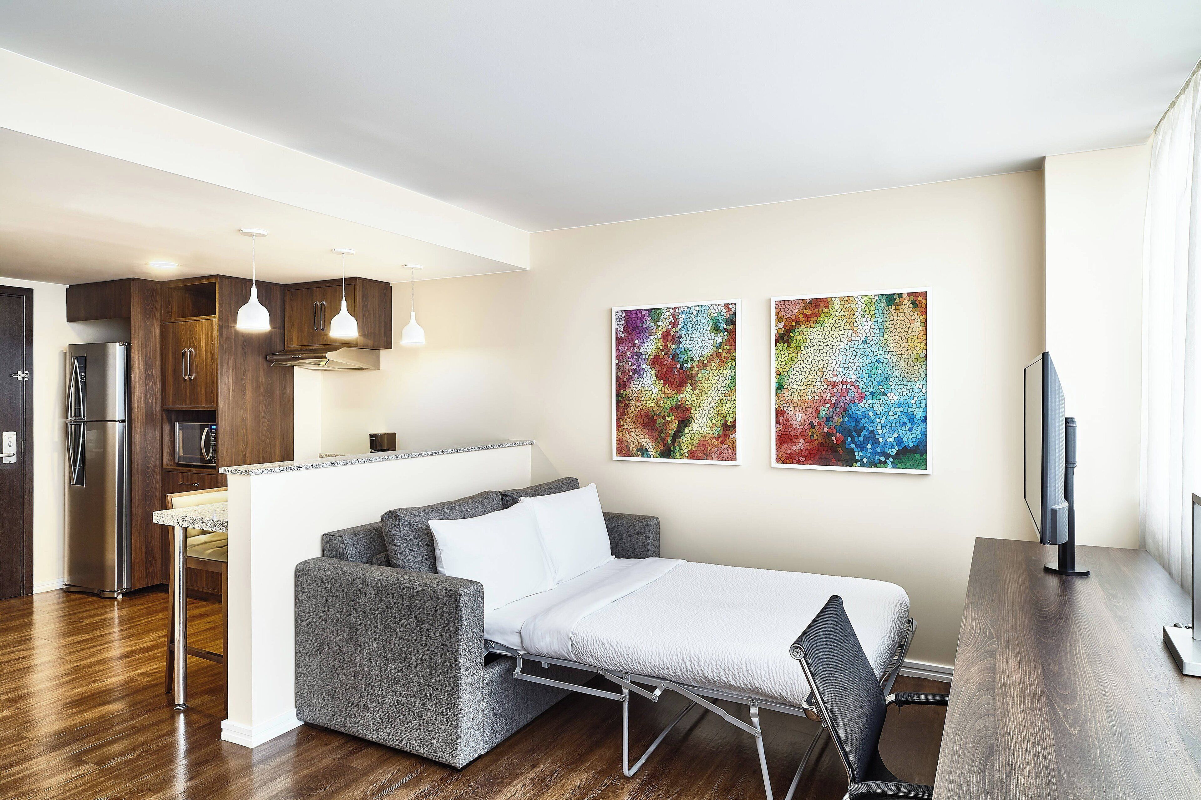 Um espaço de estar moderno com sofá-cama, área de refeições, cozinha equipada com frigorífico e obras de arte na parede.