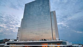 Um hotel moderno em arranha-céu com fachada de vidro refletivo, área comercial no térreo e céu claro.