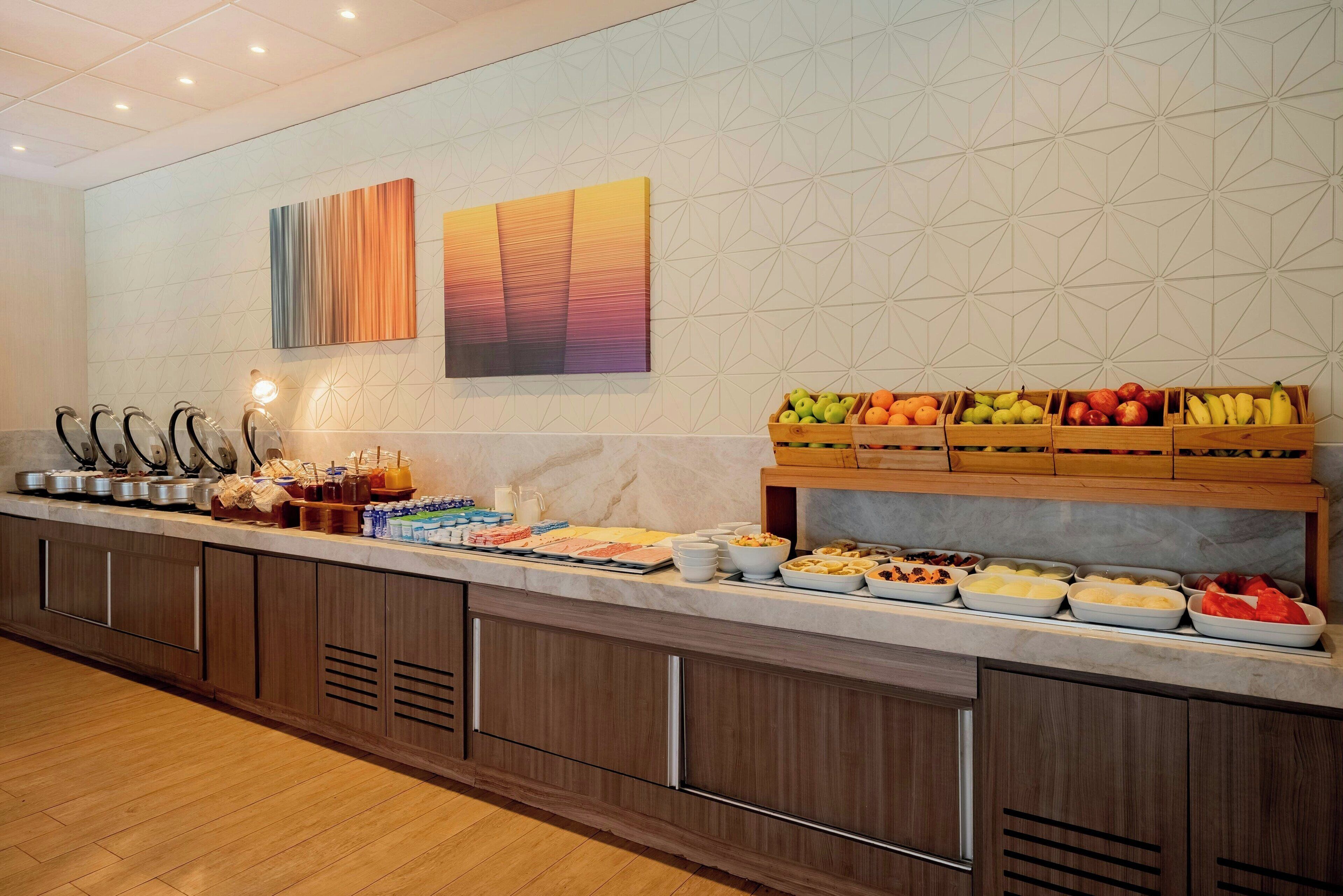 A buffet setup with various food items and beverages, wooden cabinets, and a geometric patterned wall.
