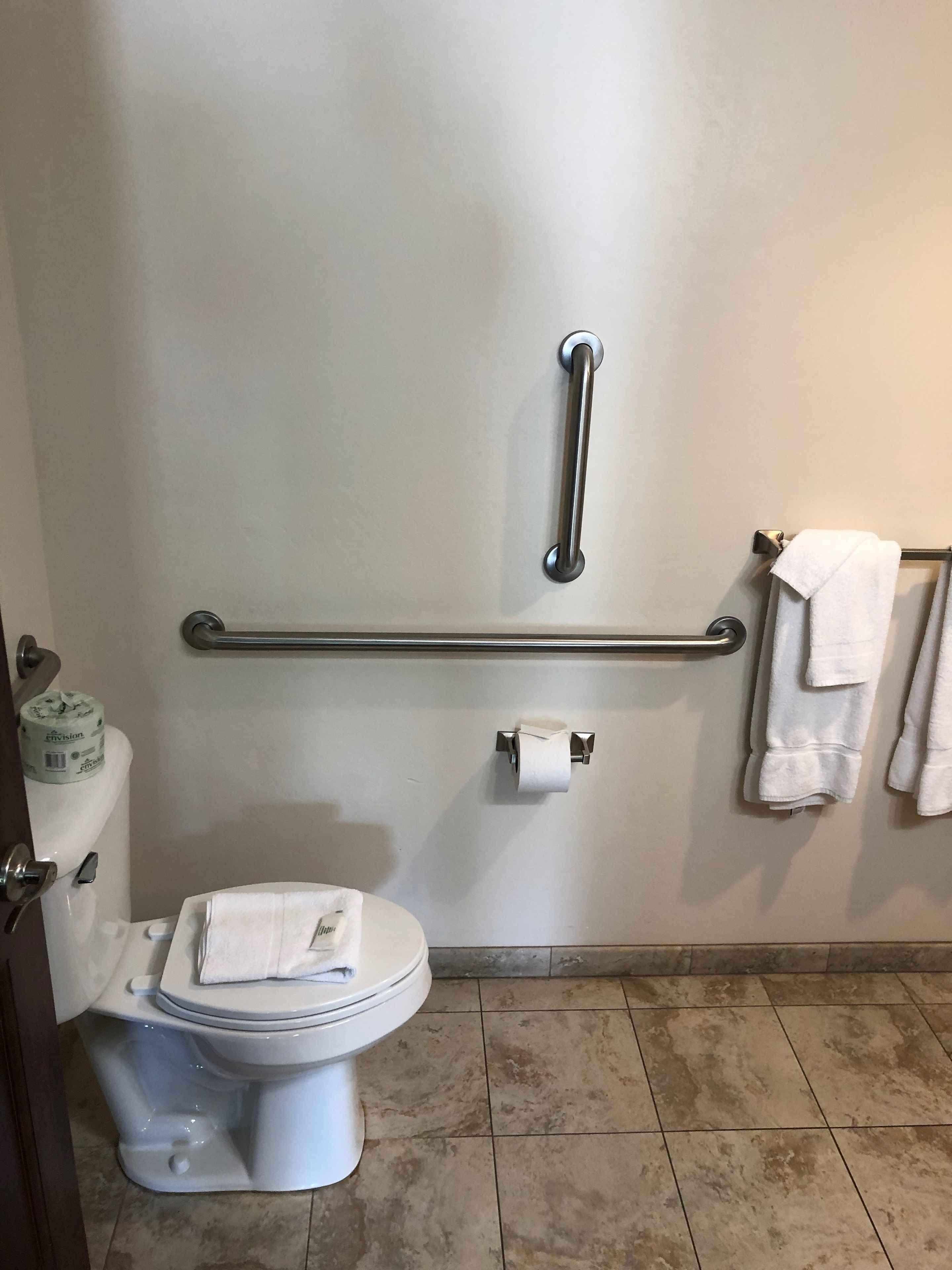 A bathroom with a toilet, a grab bar, a towel rack, and toilet paper.