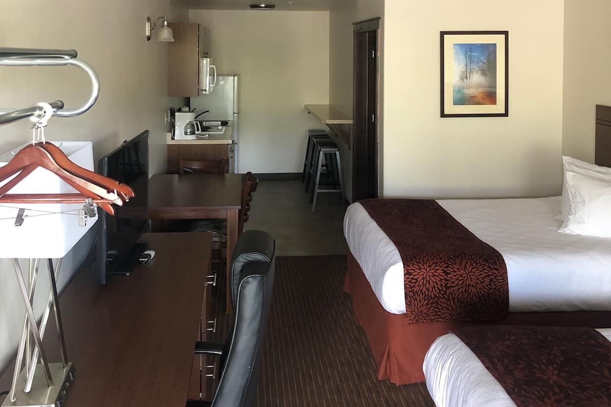 Una habitación de hotel con cama, escritorio, silla, perchero y televisor.