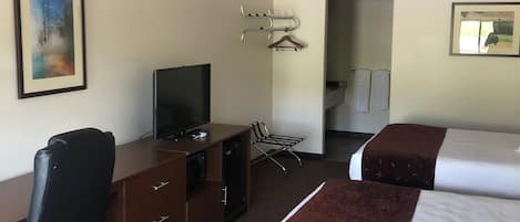 Ein Hotelzimmer mit Bett, Schreibtisch mit Stuhl, Fernseher, Kleiderständer und einem durch eine offene Tür einsehbaren Badezimmer.