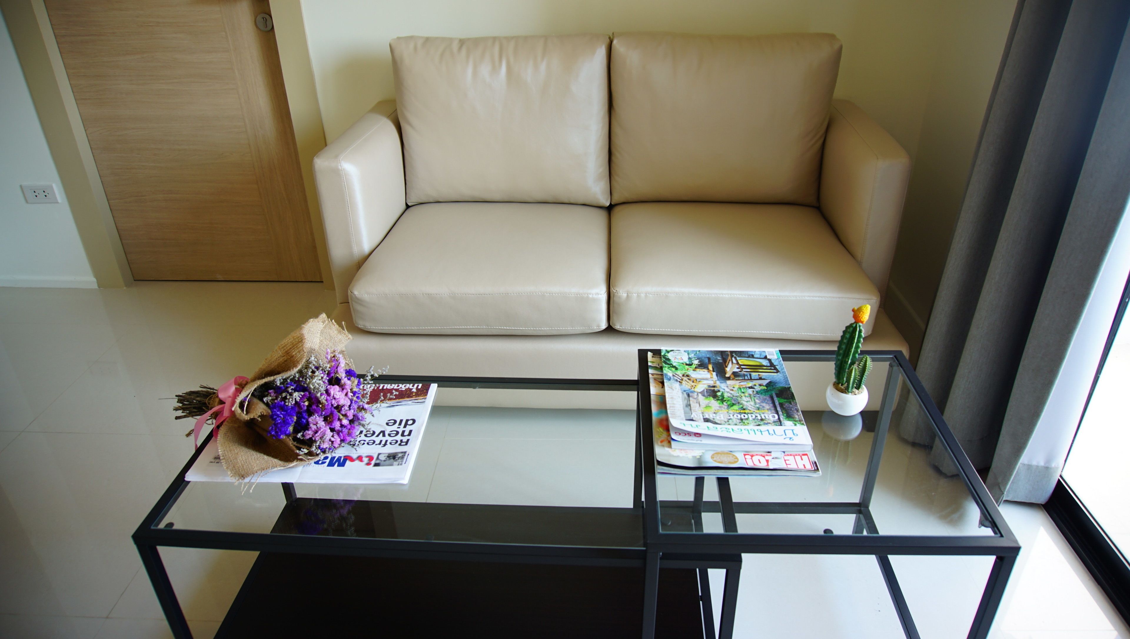 Ein Wohnzimmer mit einem beigefarbenen Sofa, einem Glastisch, einem kleinen Sukkulenten im Topf und einem Blumenstrauß.