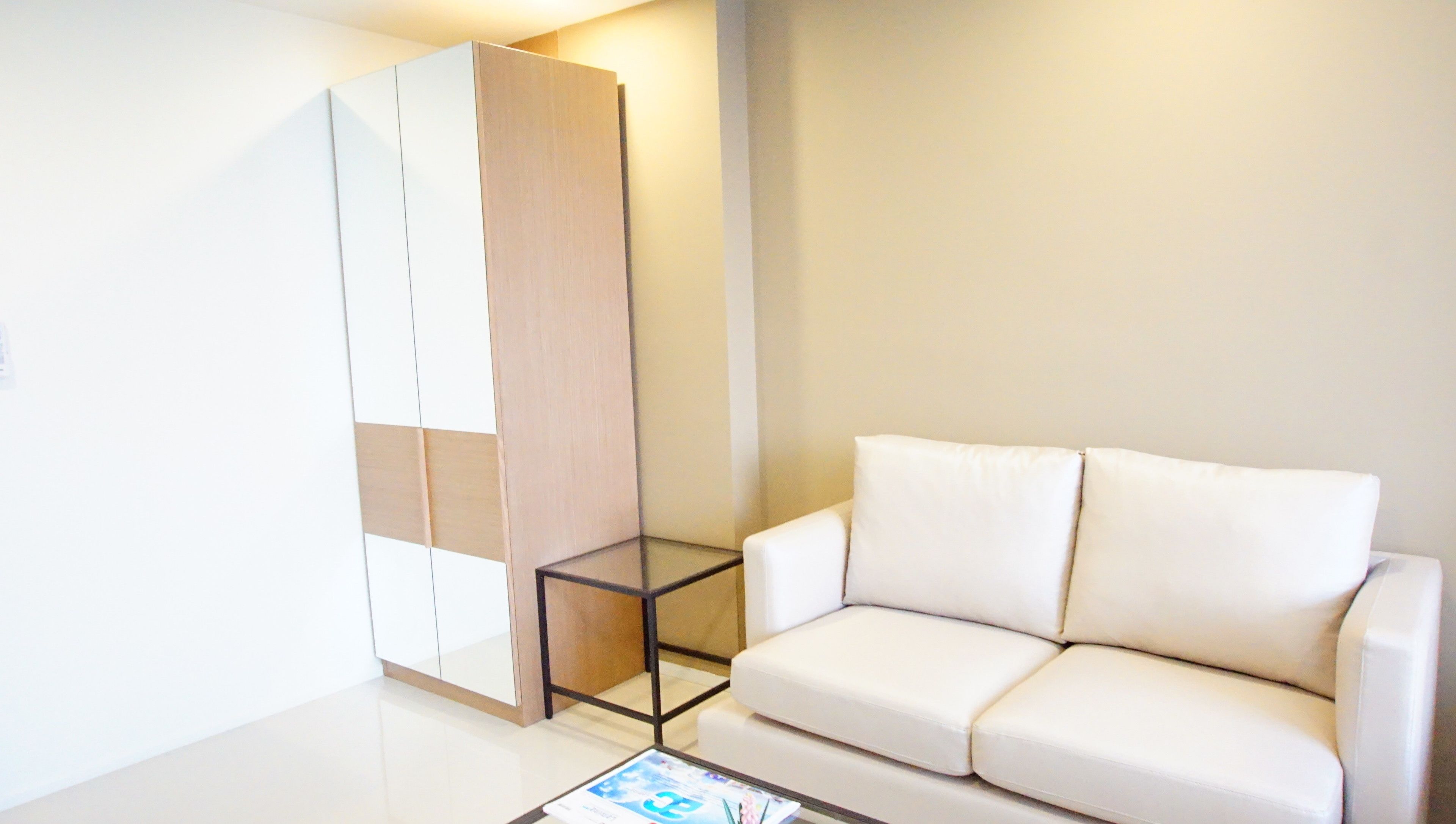 A modern living room with a white sofa, a glass coffee table, and a wooden wardrobe.