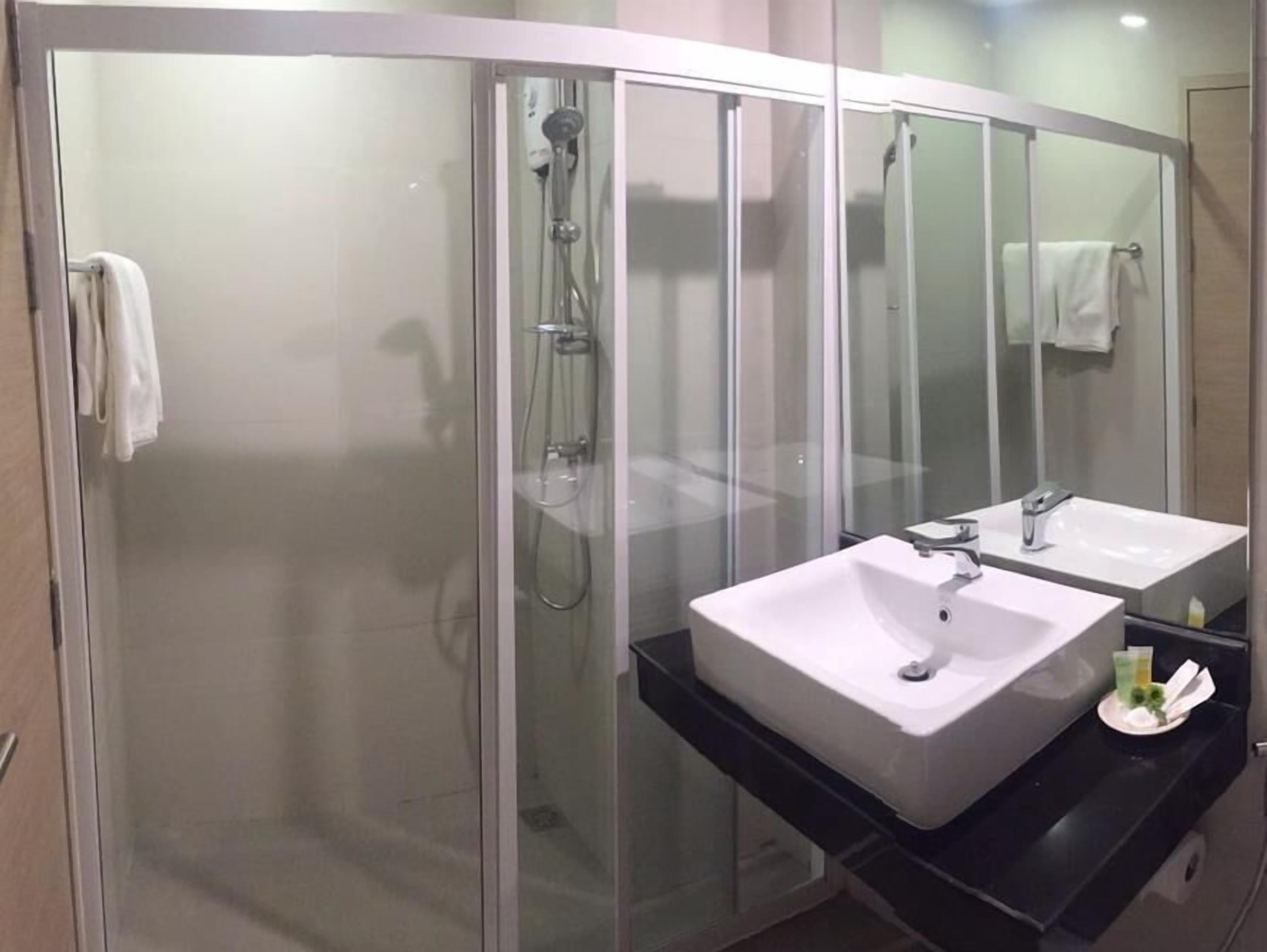 Un baño moderno con ducha de vidrio, dos lavamanos y un espejo grande.