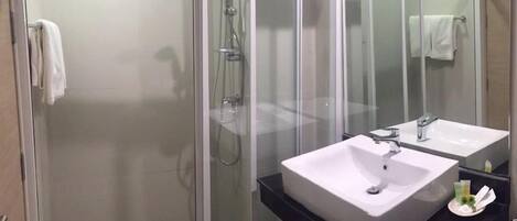 Un baño moderno con ducha de vidrio, dos lavamanos y un espejo grande.