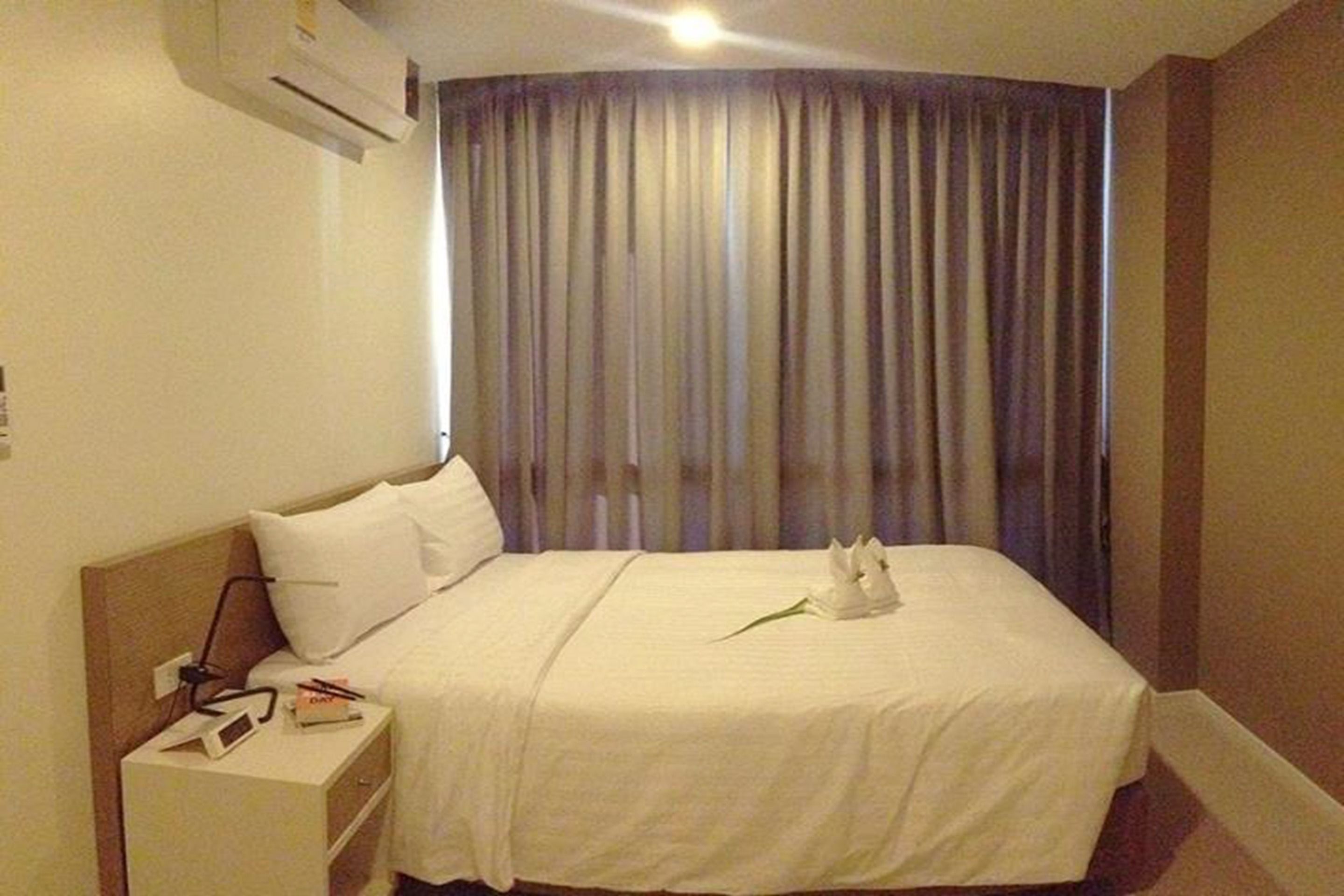 Une chambre d’hôtel avec un lit, une table de chevet et une fenêtre avec des rideaux.