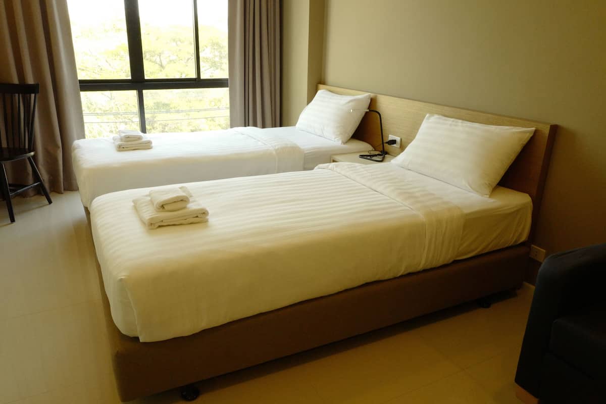 A hotel room with two beds, a chair, and a window with curtains.