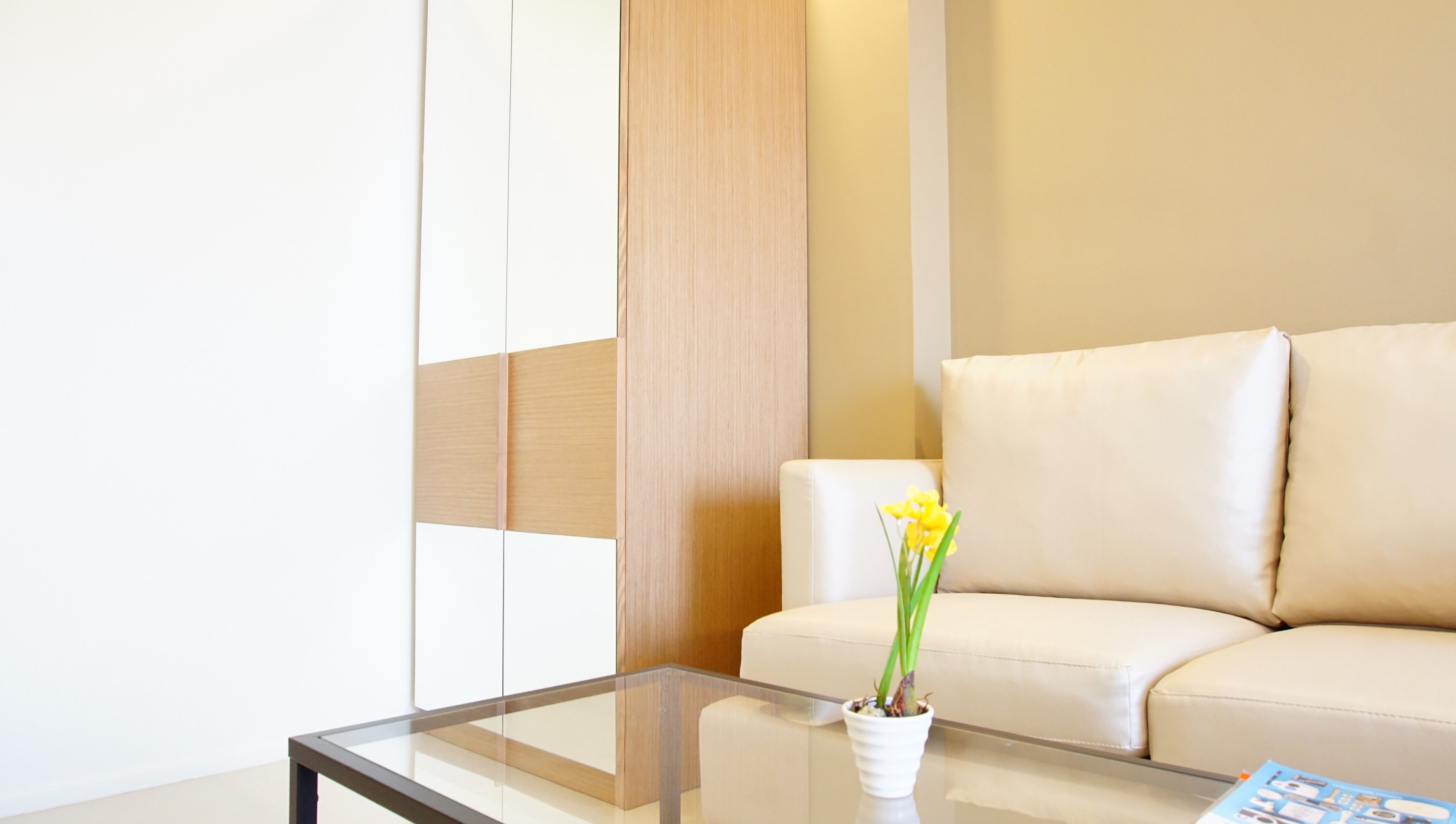Una sala de estar moderna con una mesa de centro de vidrio, un sofá color beige y un jarrón blanco con flores amarillas.