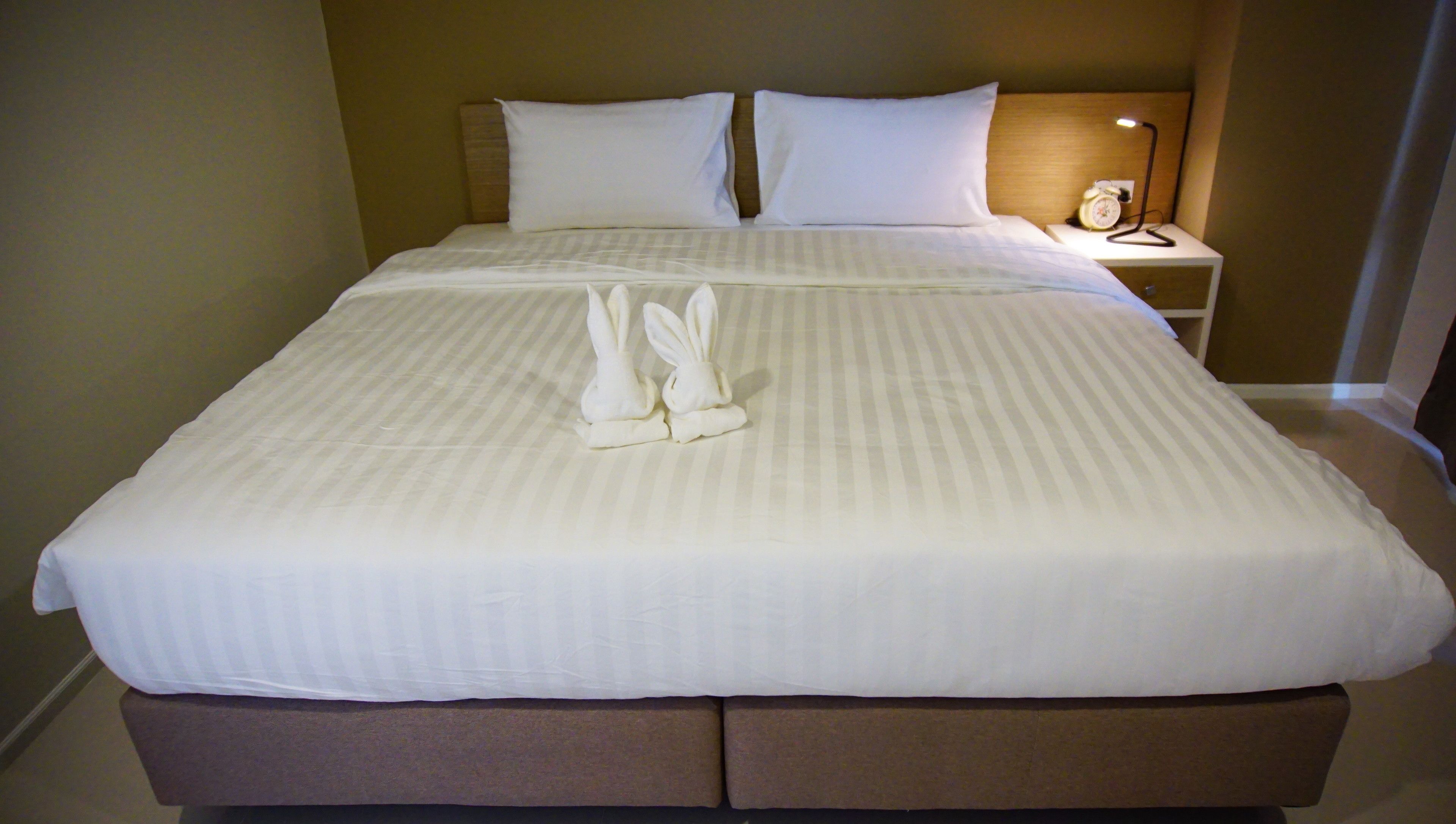 A neatly made bed with a striped bedspread, two pillows, and a pair of white towels arranged in bunny shapes.