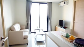 A modern hotel room with a sofa, a small table, a TV, and a dining area with plates and cups. - 185 Residence (Khon Kaen)