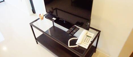 A glass-top table with a flat-screen TV, a remote control, and a white telephone.