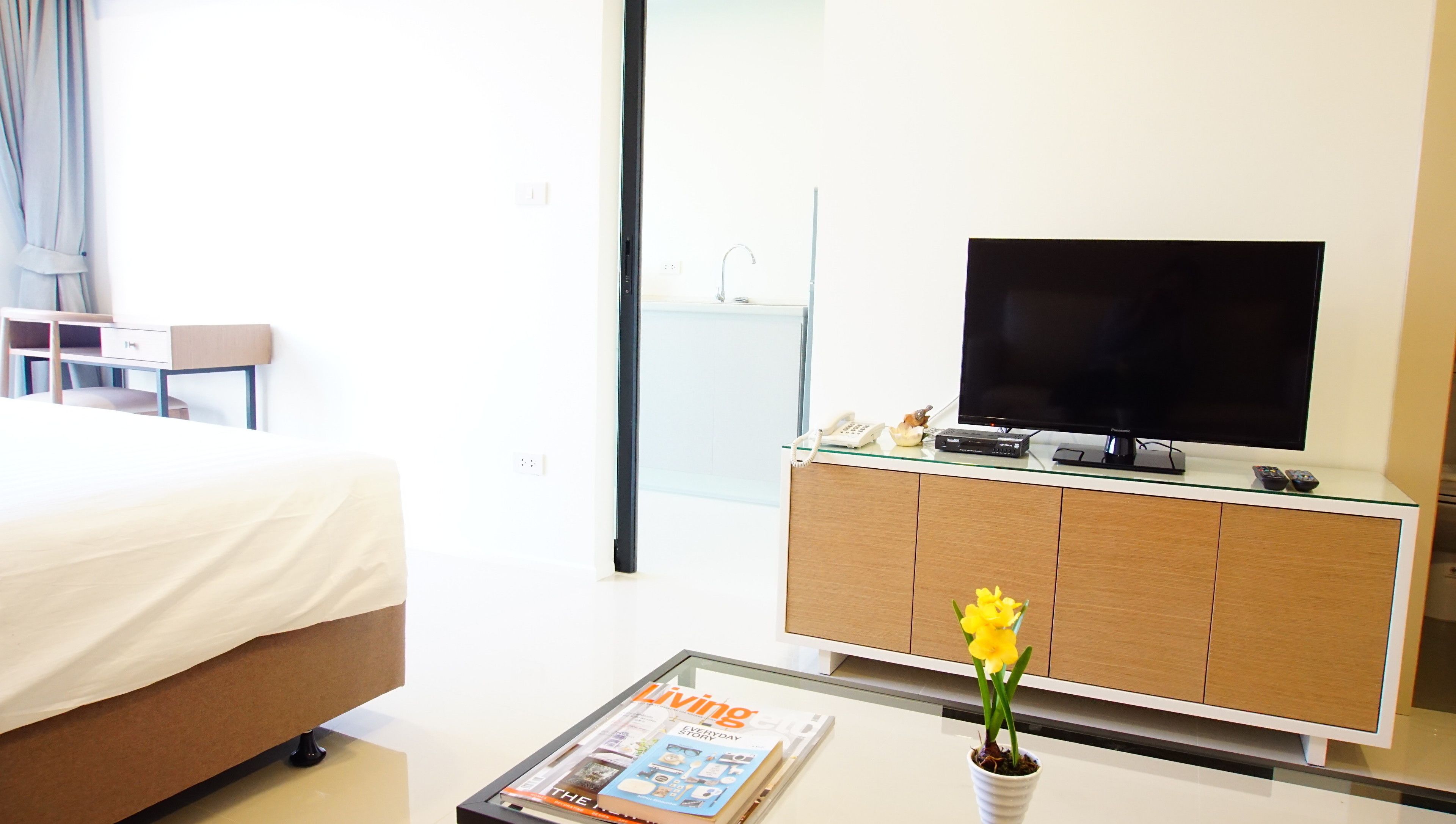A hotel room with a bed, a TV on a wooden cabinet, a magazine on a table, and a flower vase.