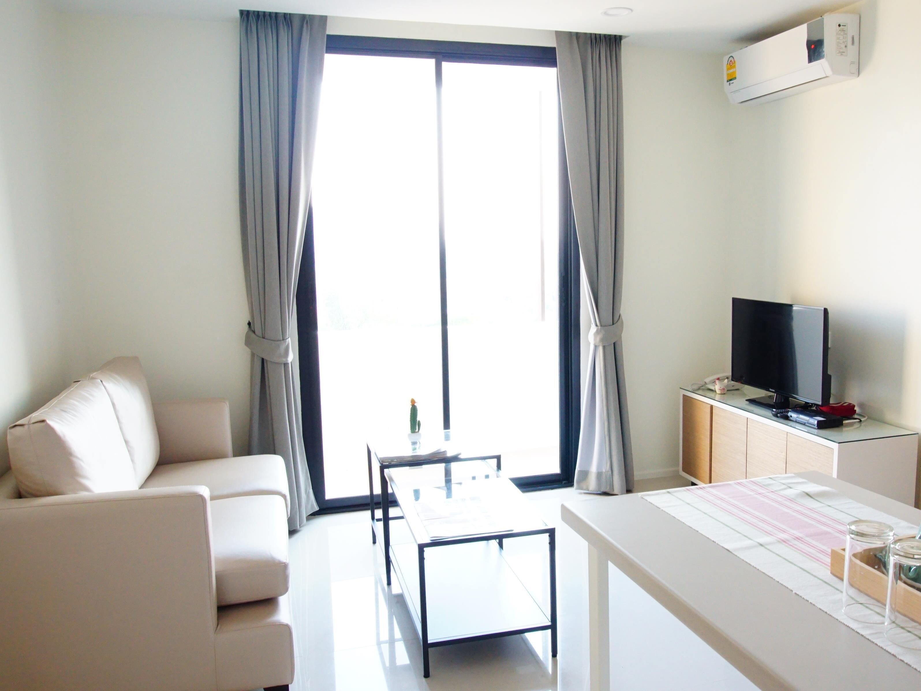 A modern hotel room with a sofa, a small table, a TV, and a window with curtains.
