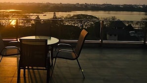 A terrace with a table and chairs, overlooking a river and cityscape during sunset. - 185 Residence (Khon Kaen)