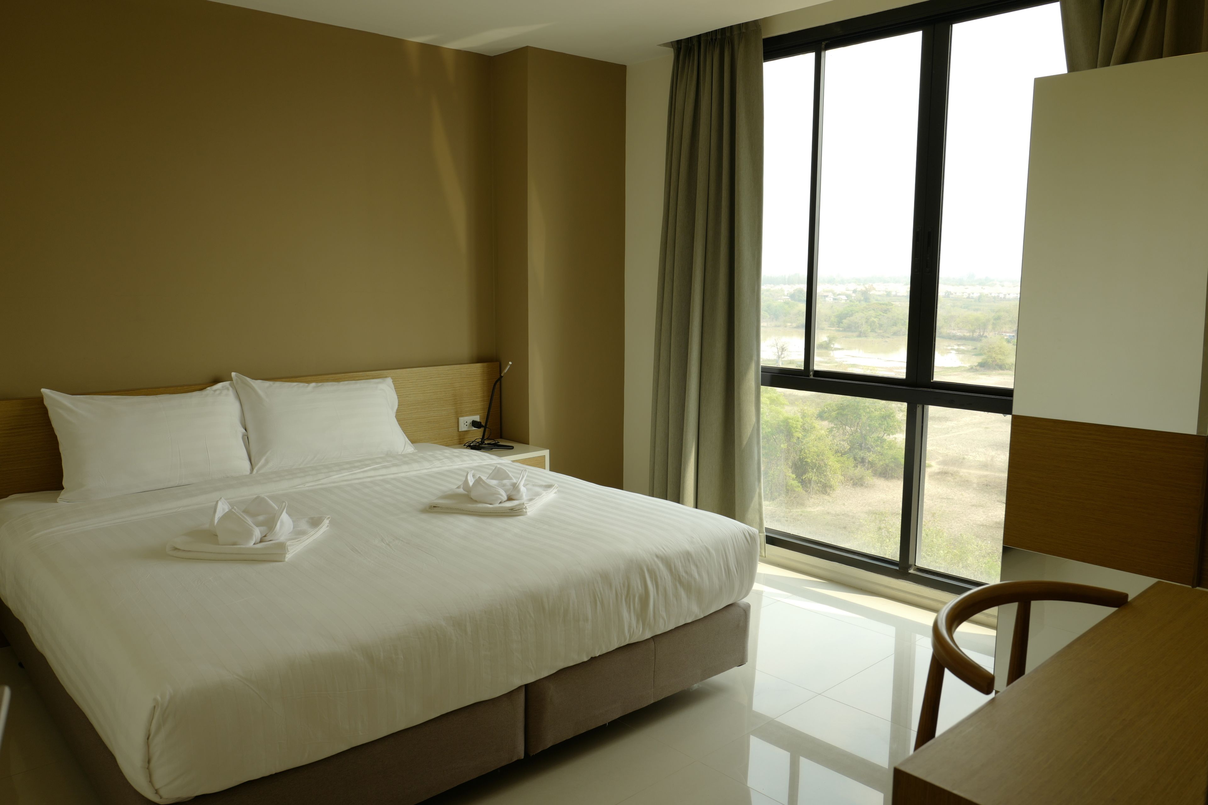 A hotel room with a large bed, a desk, and a view of the outdoors through a window.
