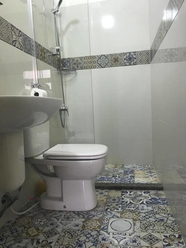 A bathroom with a toilet, a sink, and a shower. The floor has patterned tiles, and the walls are tiled with a mix of plain and patterned tiles. - Zaman Ya Zaman Boutique Hotel (Amman)