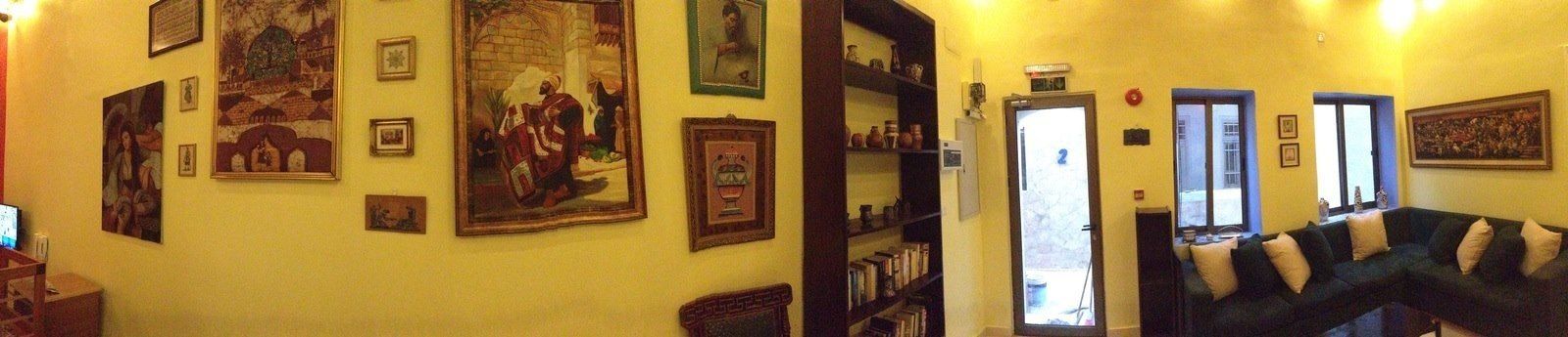 A room with a large bookshelf, a dark green sofa, and various framed pictures on the walls.