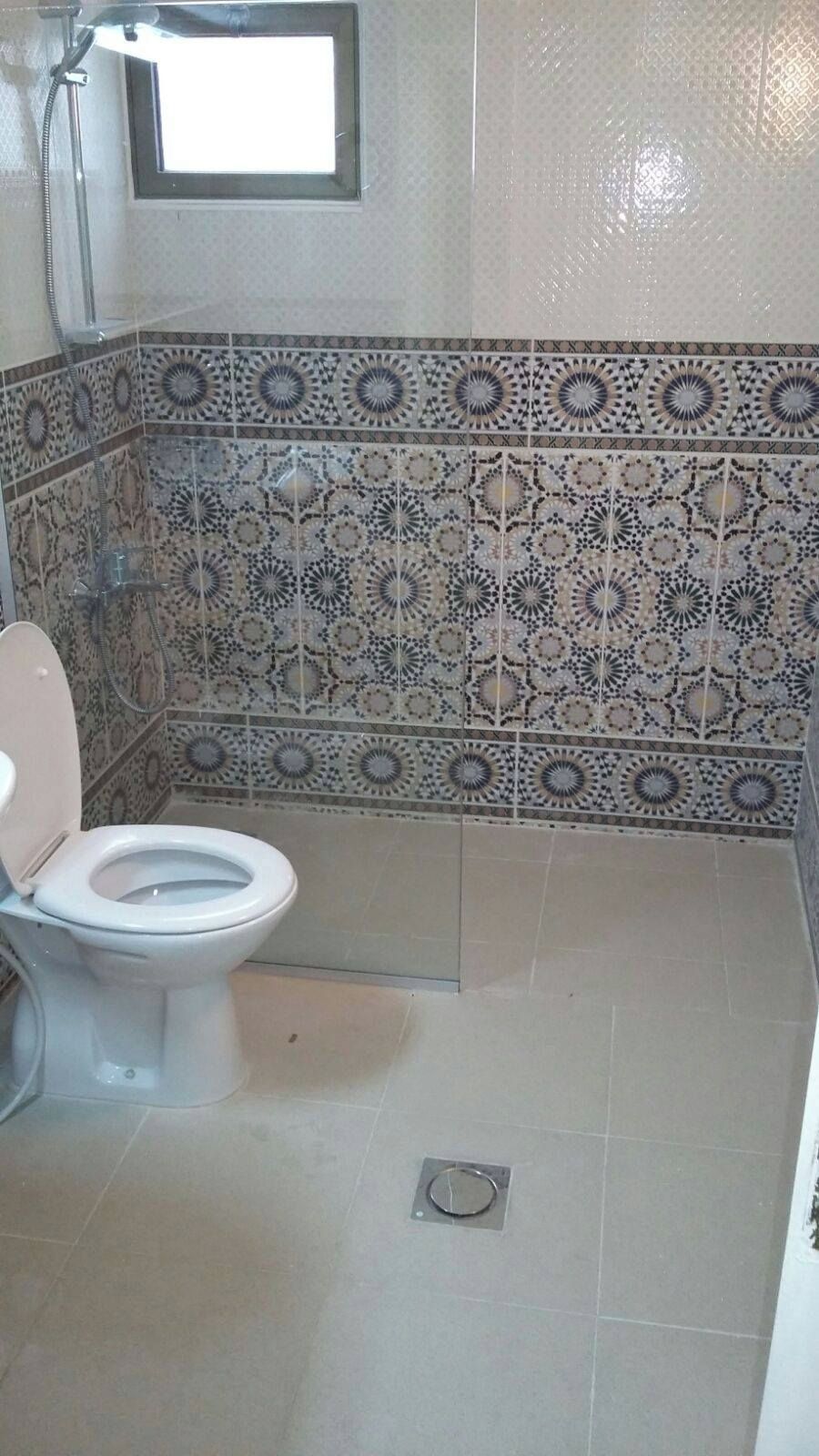 A bathroom with a toilet, shower, and decorative tiled walls.