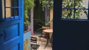 Un patio estrecho con una puerta azul, una mesa pequeña y sillas.