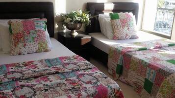A hotel room with two beds, floral-patterned bedding, a nightstand with a vase of flowers, and wall-mounted lamps.