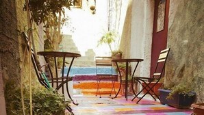 Un conjunto de escalones coloridos que conducen a un área de descanso con dos mesas y sillas, rodeada de plantas en macetas.