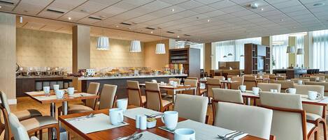 Amplia sala de comedor de hotel con múltiples mesas y sillas, un bufé central y un diseño de techo moderno.