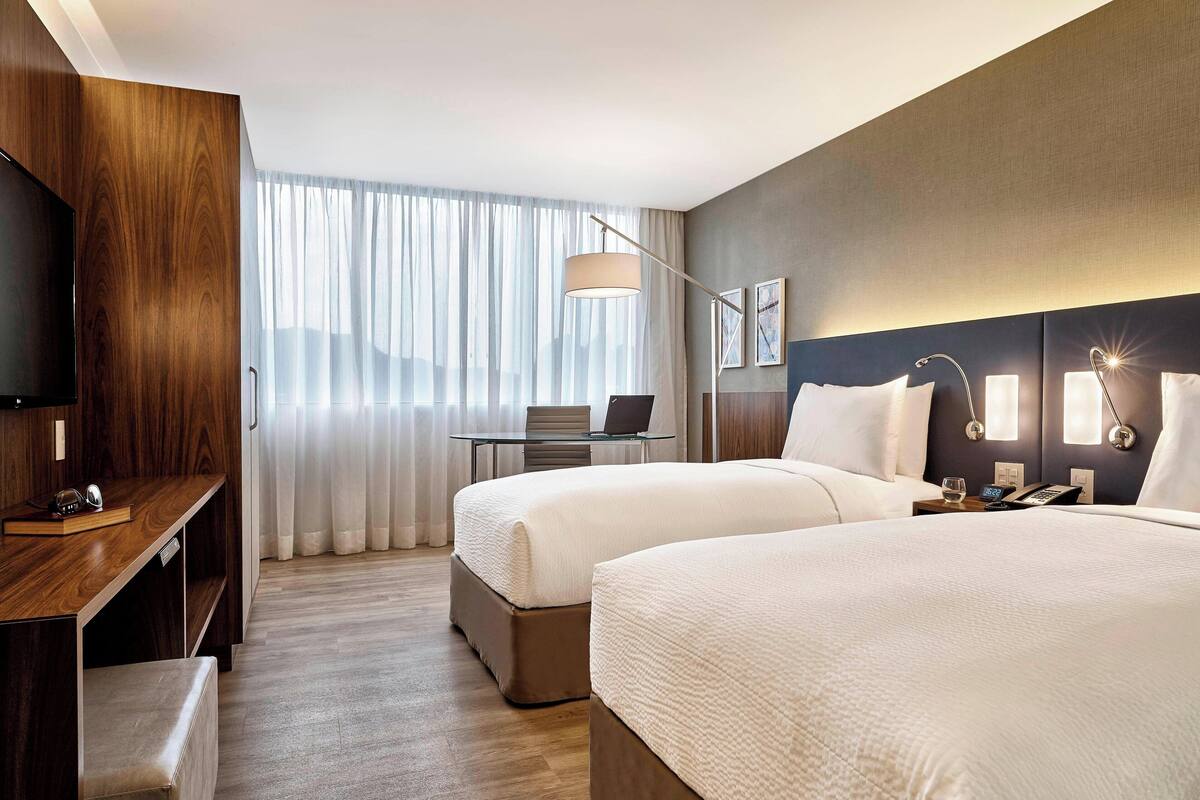 A hotel room with two beds, a desk, a laptop, and a TV.