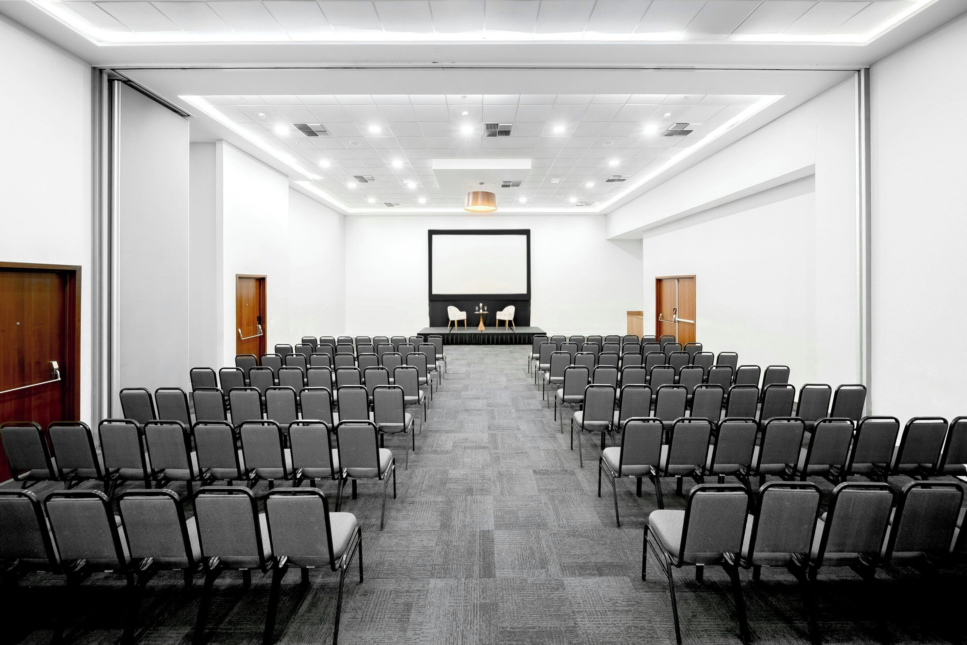A conference room with rows of chairs, a podium, and a large screen.