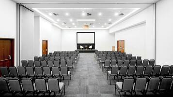 A conference room with rows of chairs, a podium, and a large screen.