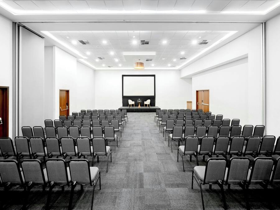 A conference room with rows of chairs, a podium, and a large screen.