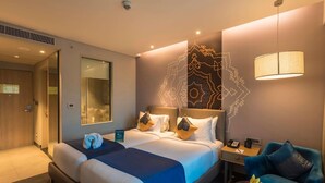 A hotel room with a large bed, a desk with a lamp, a chair, and a small table with fruit. - Grand Mercure Mysore (Mysore)