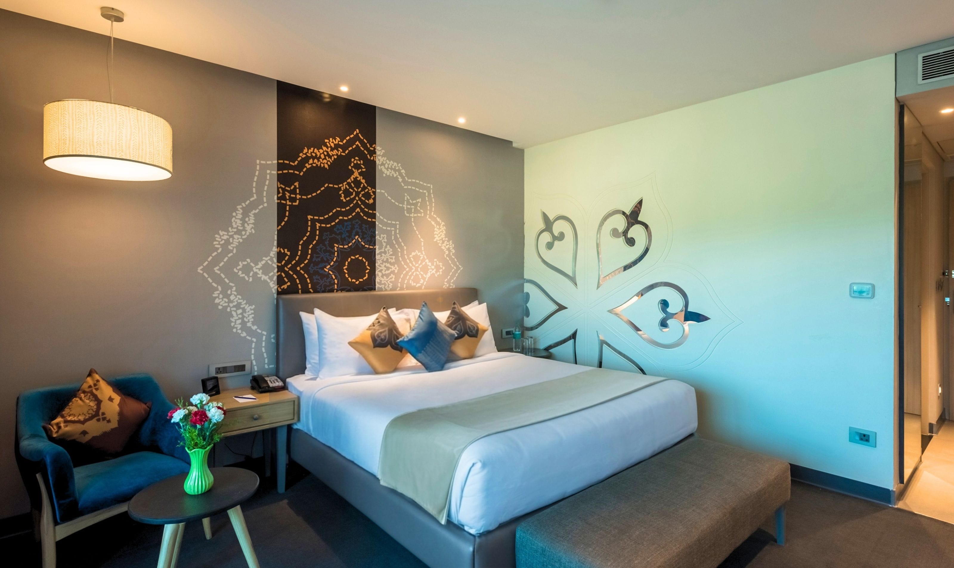 A hotel room with a bed, bedside table, chair, and decorative wall art.