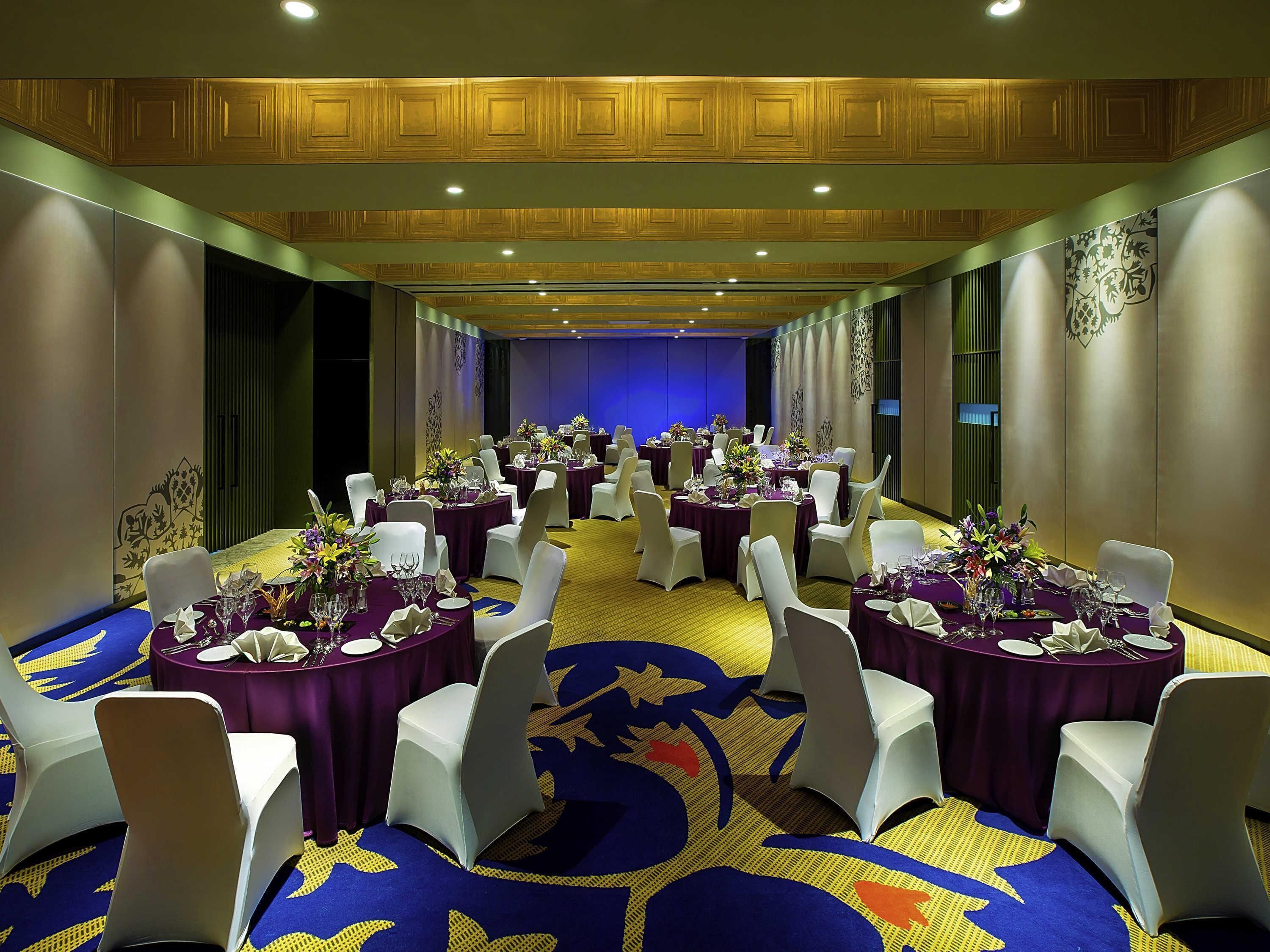 Un salón de banquetes con mesas redondas, sillas blancas y manteles morados.