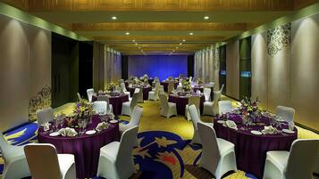 Un salón de banquetes con mesas redondas, sillas blancas y manteles morados.