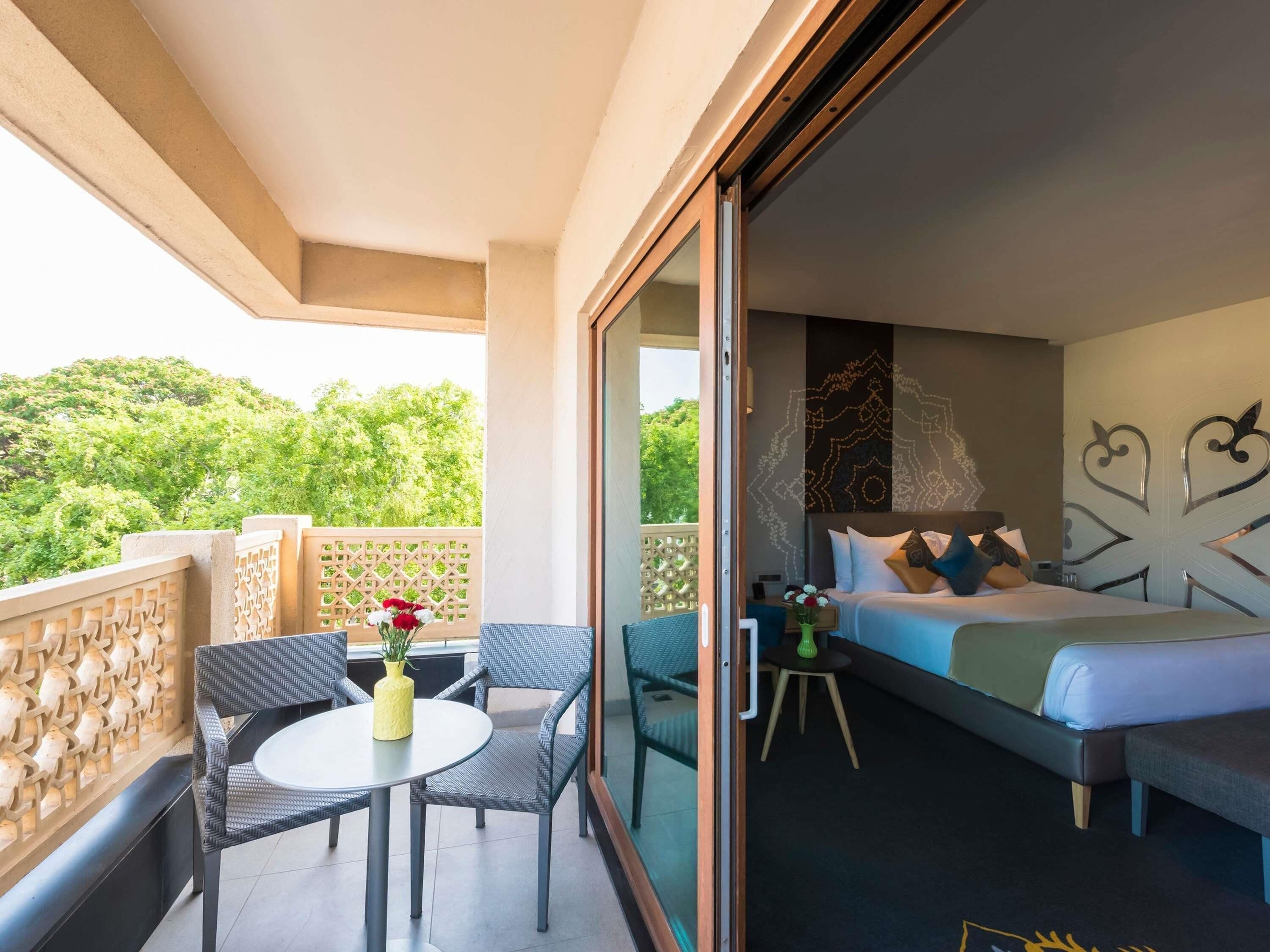 Un balcón con una mesa y sillas, una cama con almohadas y un muro decorativo.