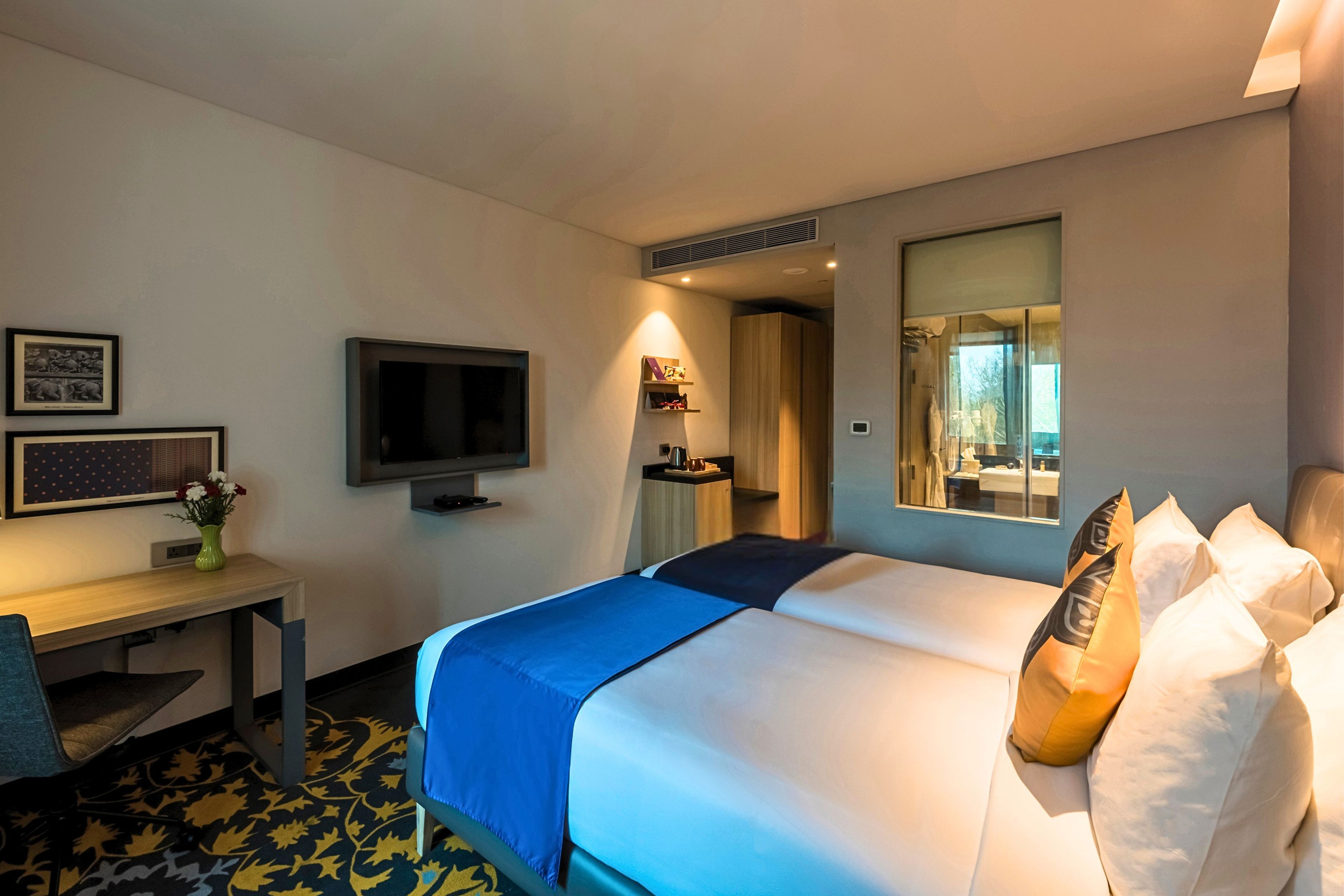 Habitación de hotel con cama, escritorio, televisor y espejo.