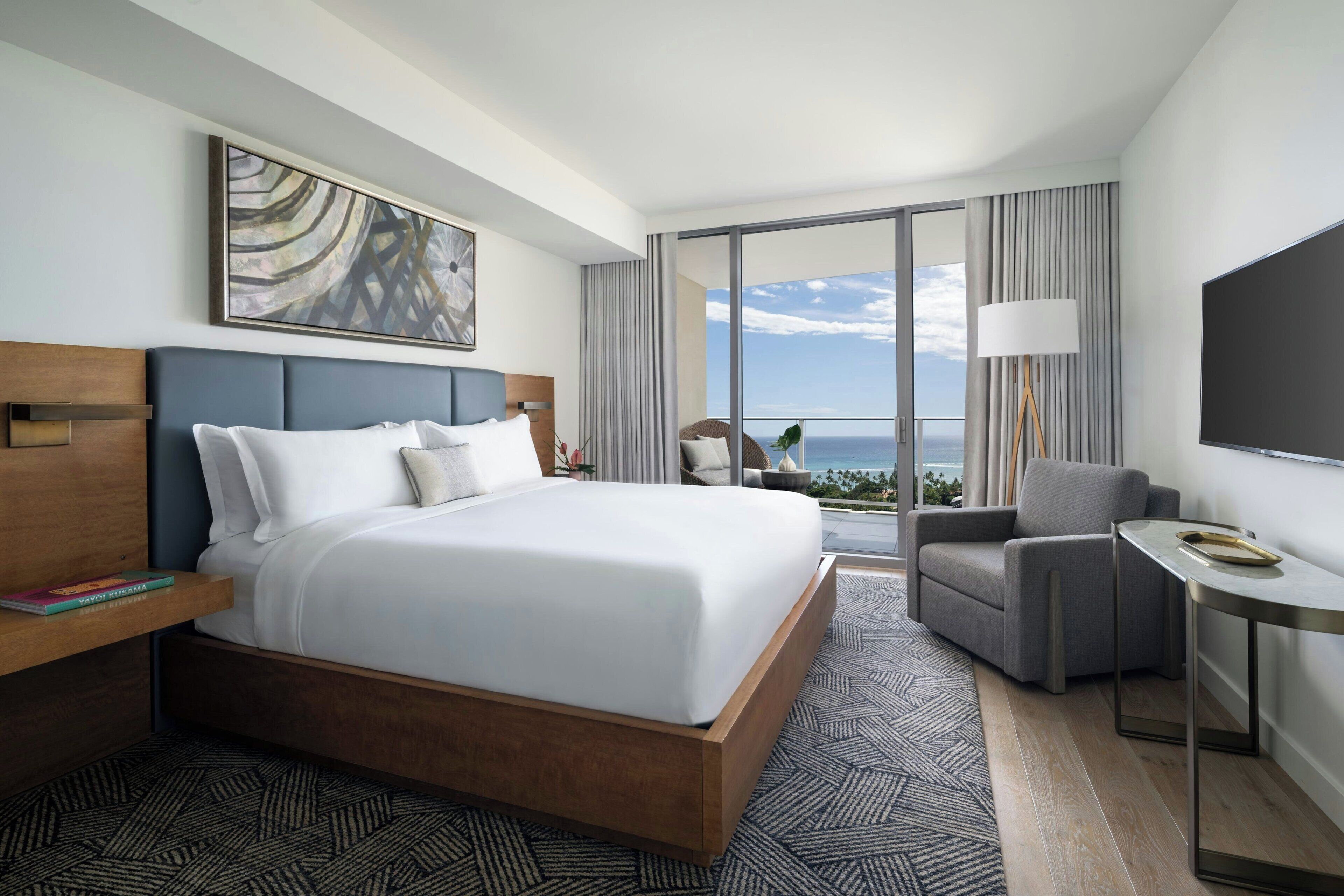 A hotel room with a large bed, a desk, a chair, a TV, and a view of the ocean.
