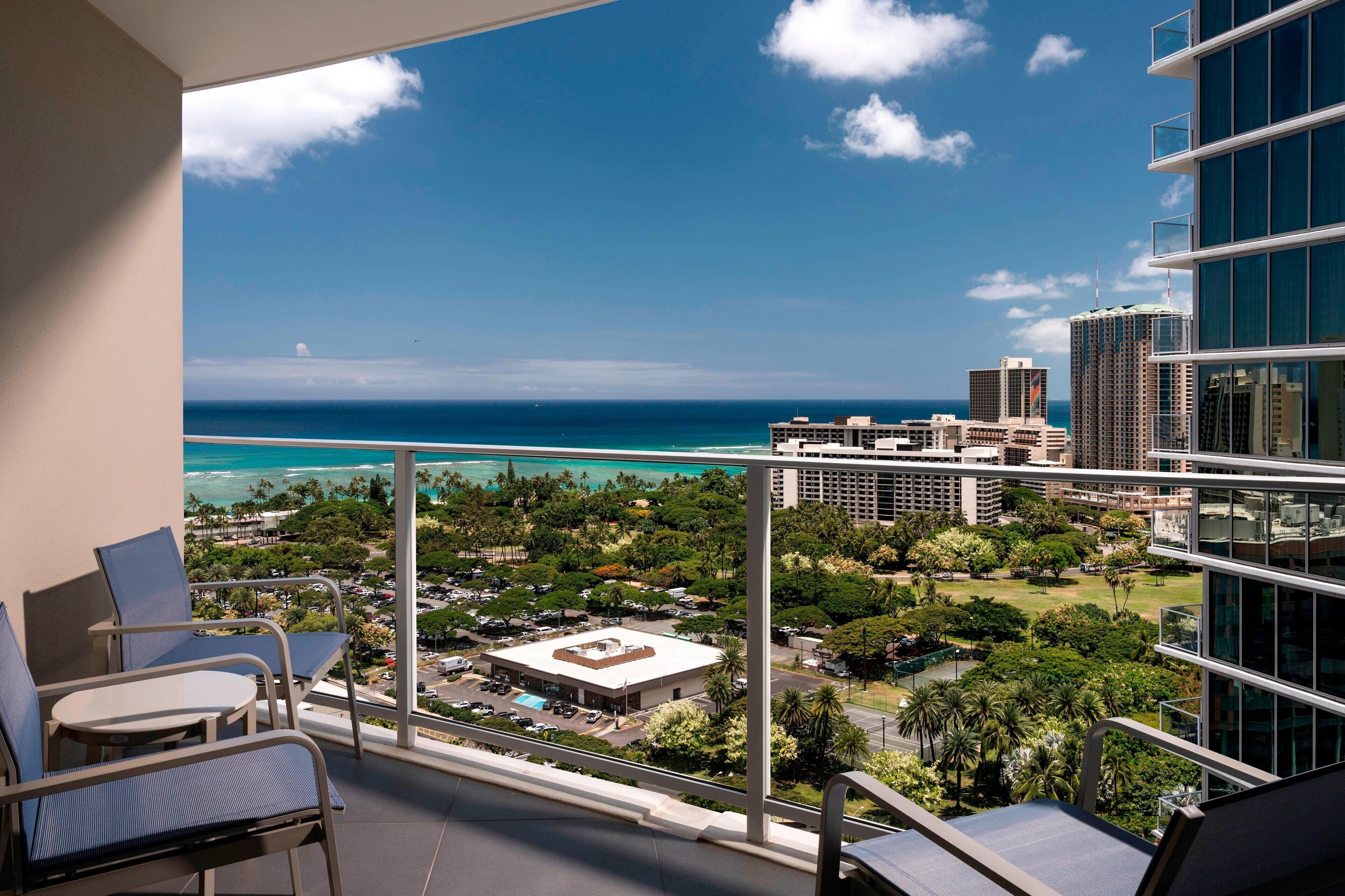 A balcony with a view of the ocean and cityscape, including high-rise buildings and a parking lot.