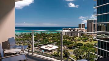 A balcony with a view of the ocean and cityscape, including high-rise buildings and a parking lot.