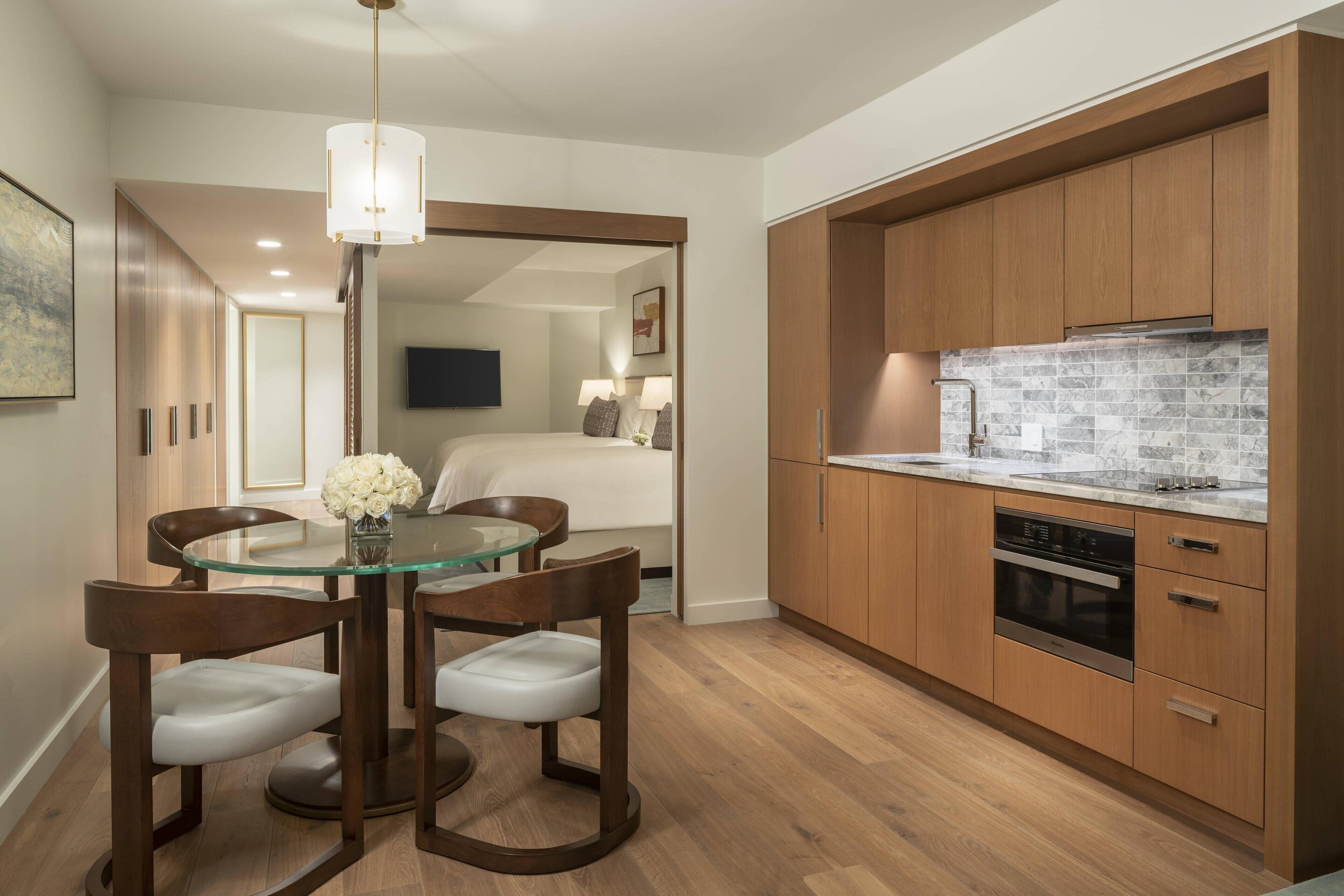 A modern kitchen with wooden cabinets, a built-in oven, and a glass dining table with chairs.